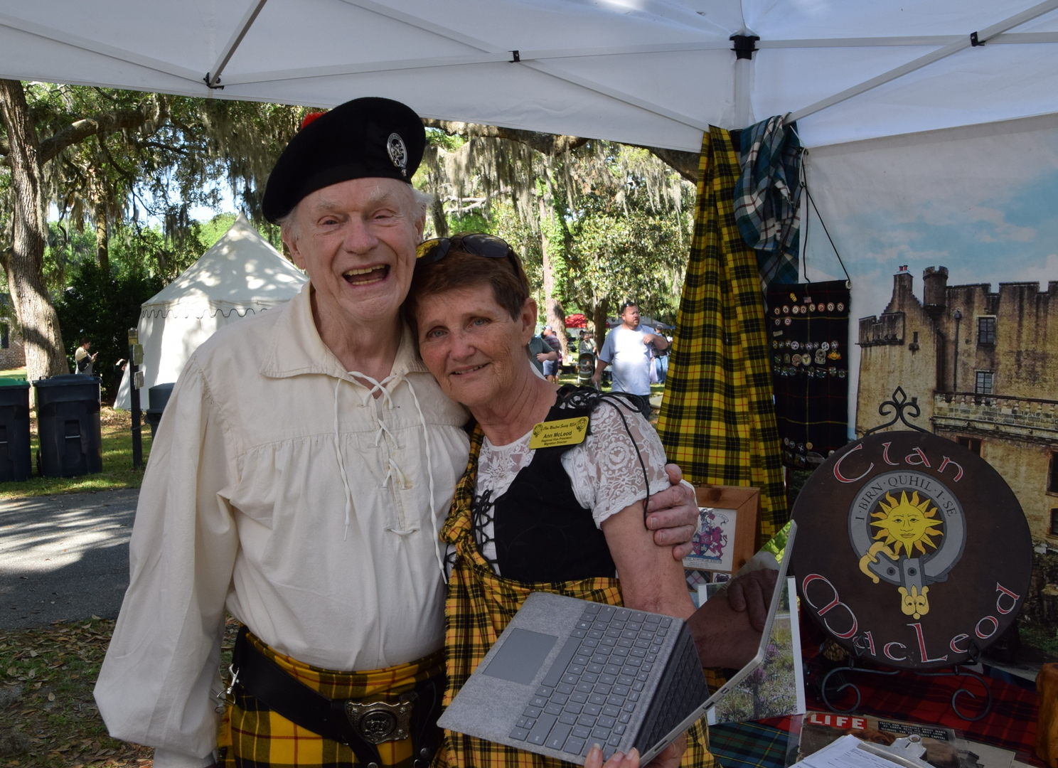 Elderly couple in Scottish attire at festival.