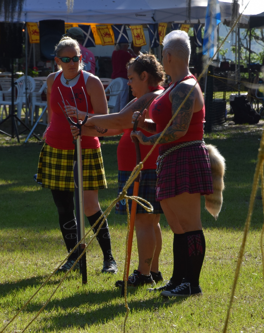 Three people in kilts holding cabers outdoors.