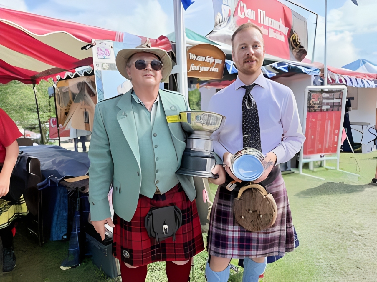 Two men in kilts holding trophies.