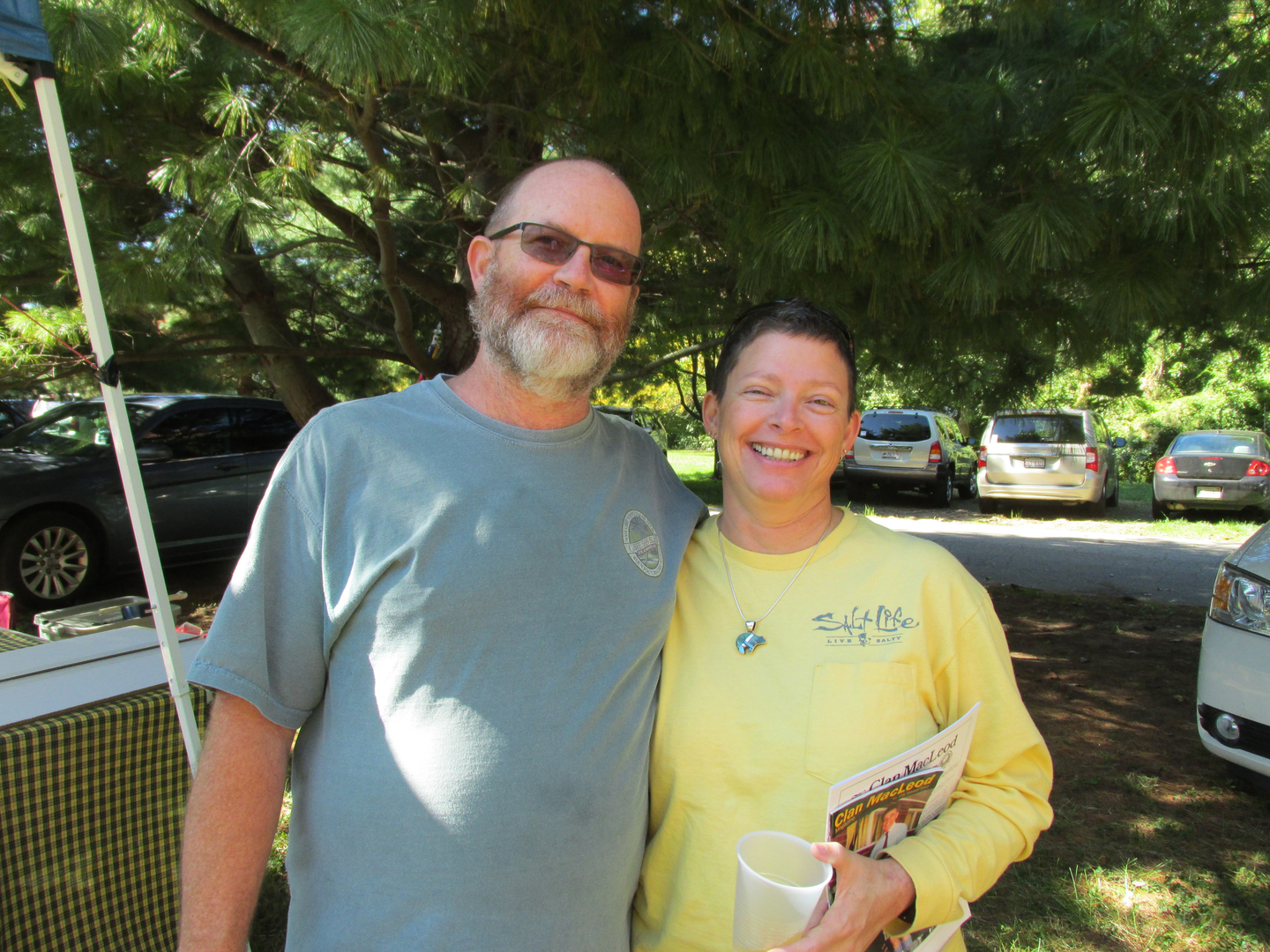 Smiling couple outdoors with trees and cars.